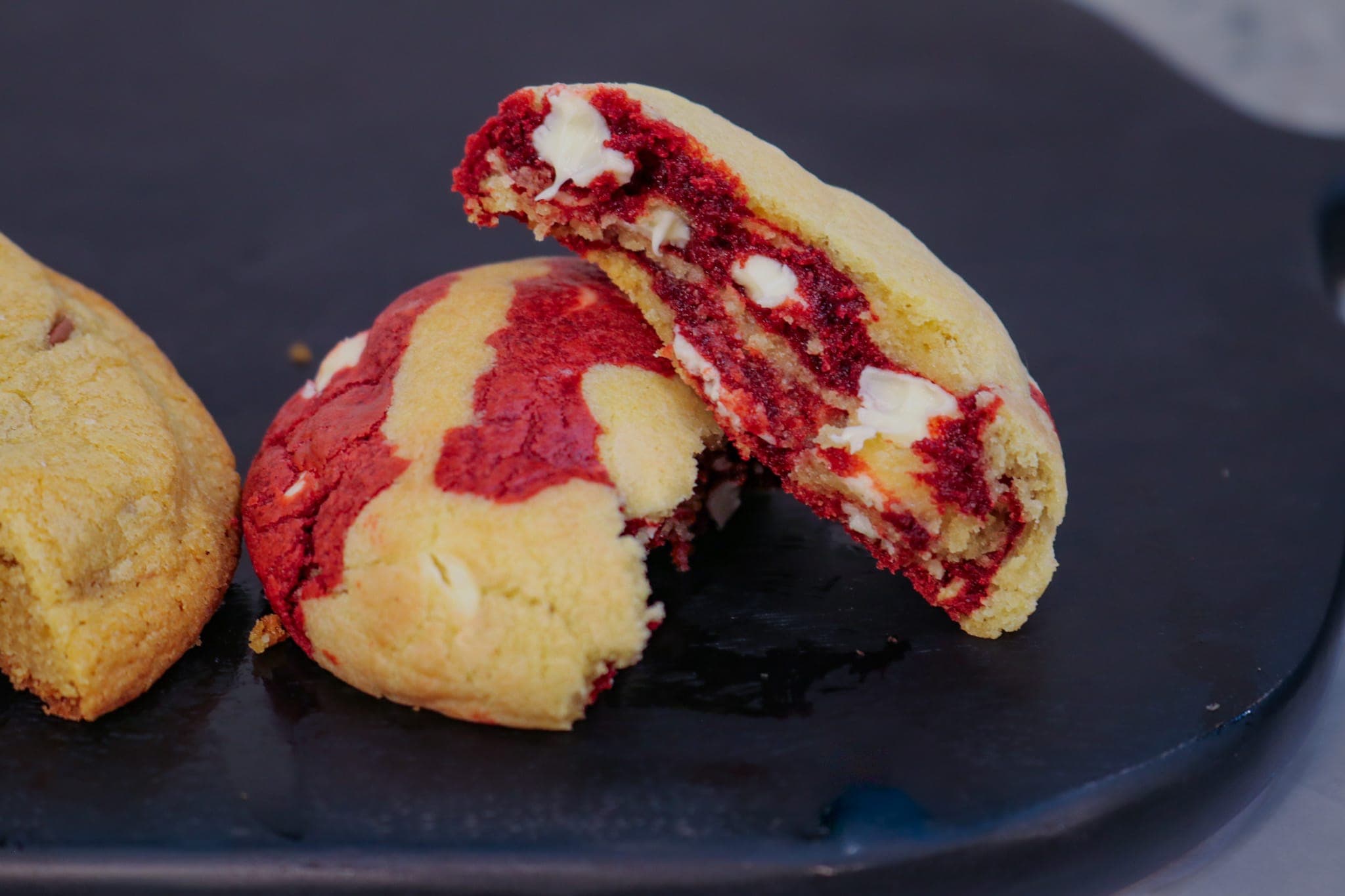 Red velvet stuffed cookie broken open to show white chocolate chunks, on black slate