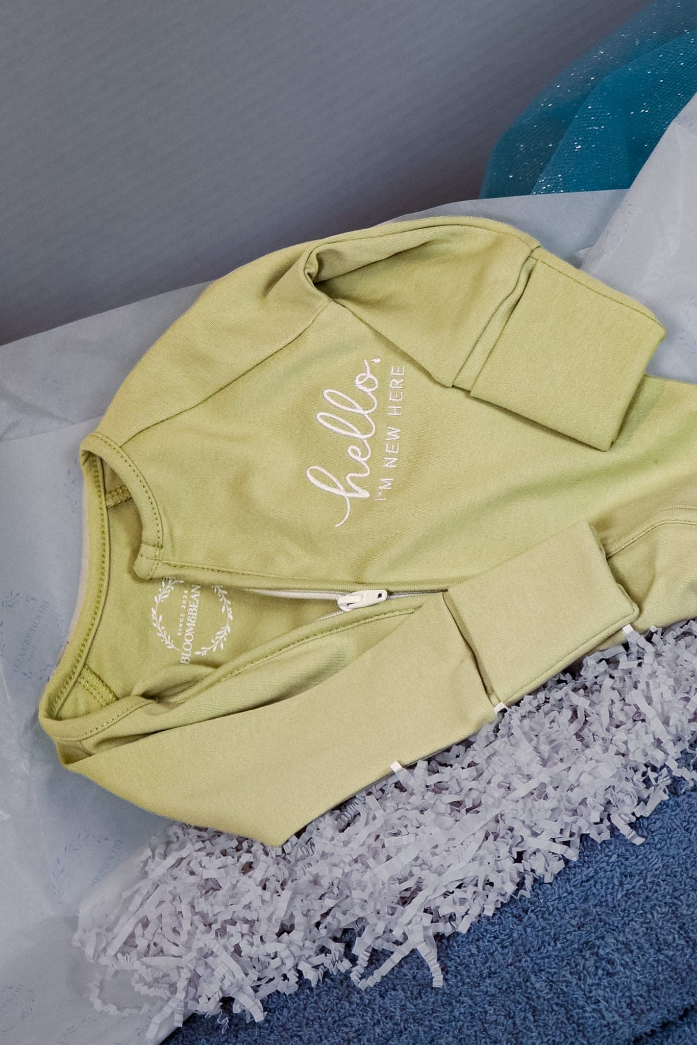 Sage green baby onesie embroidered with hello, I'm new here, laid in tissue paper
