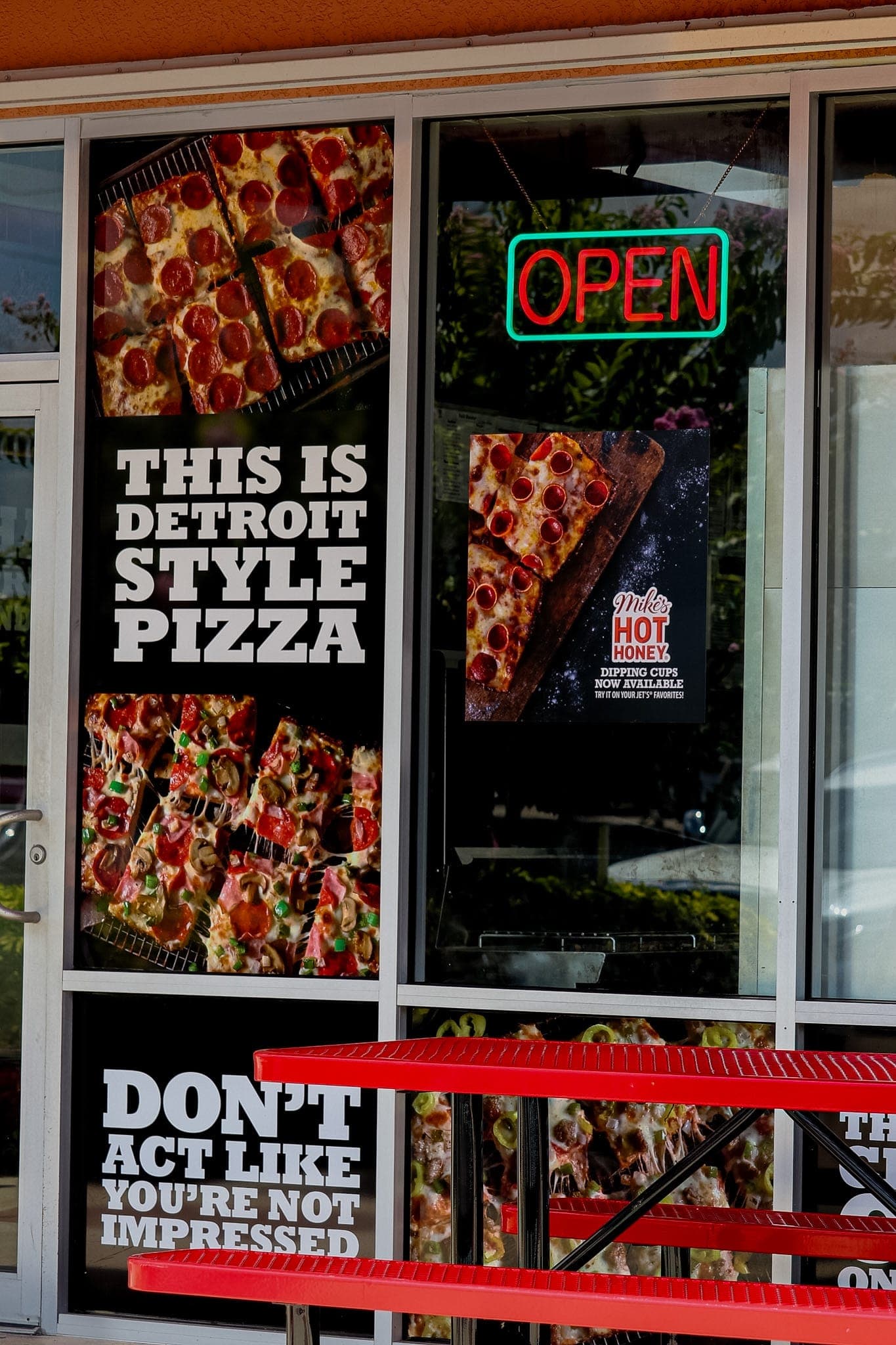 Jet's Pizza storefront with a neon OPEN sign and Detroit-style pizza window graphics