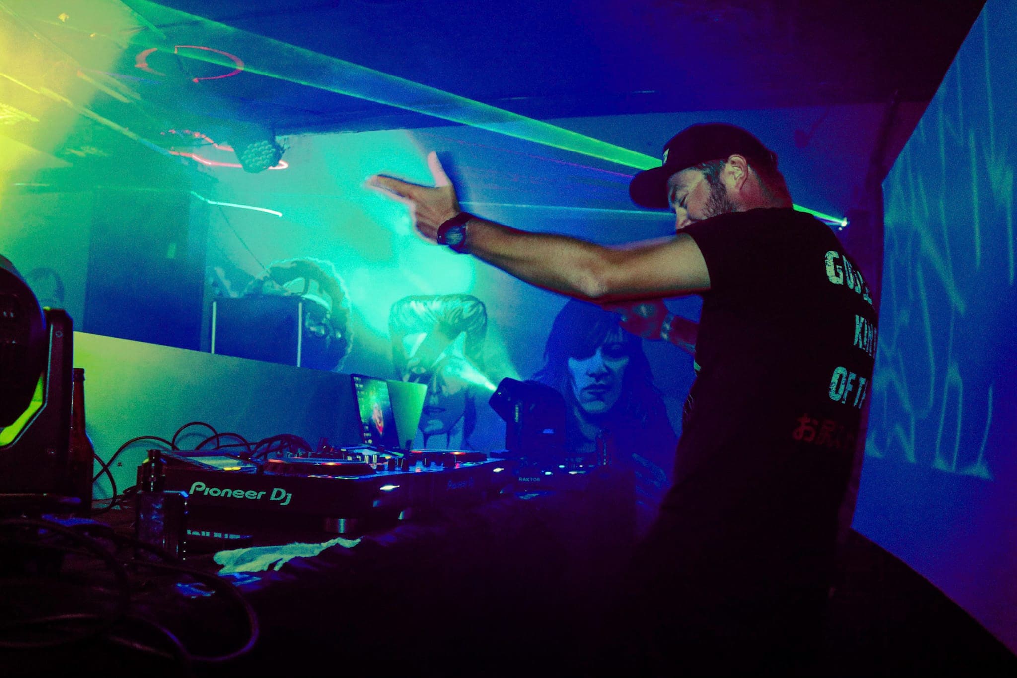 DJ throwing a hand up behind Pioneer decks as green lasers cut through the haze