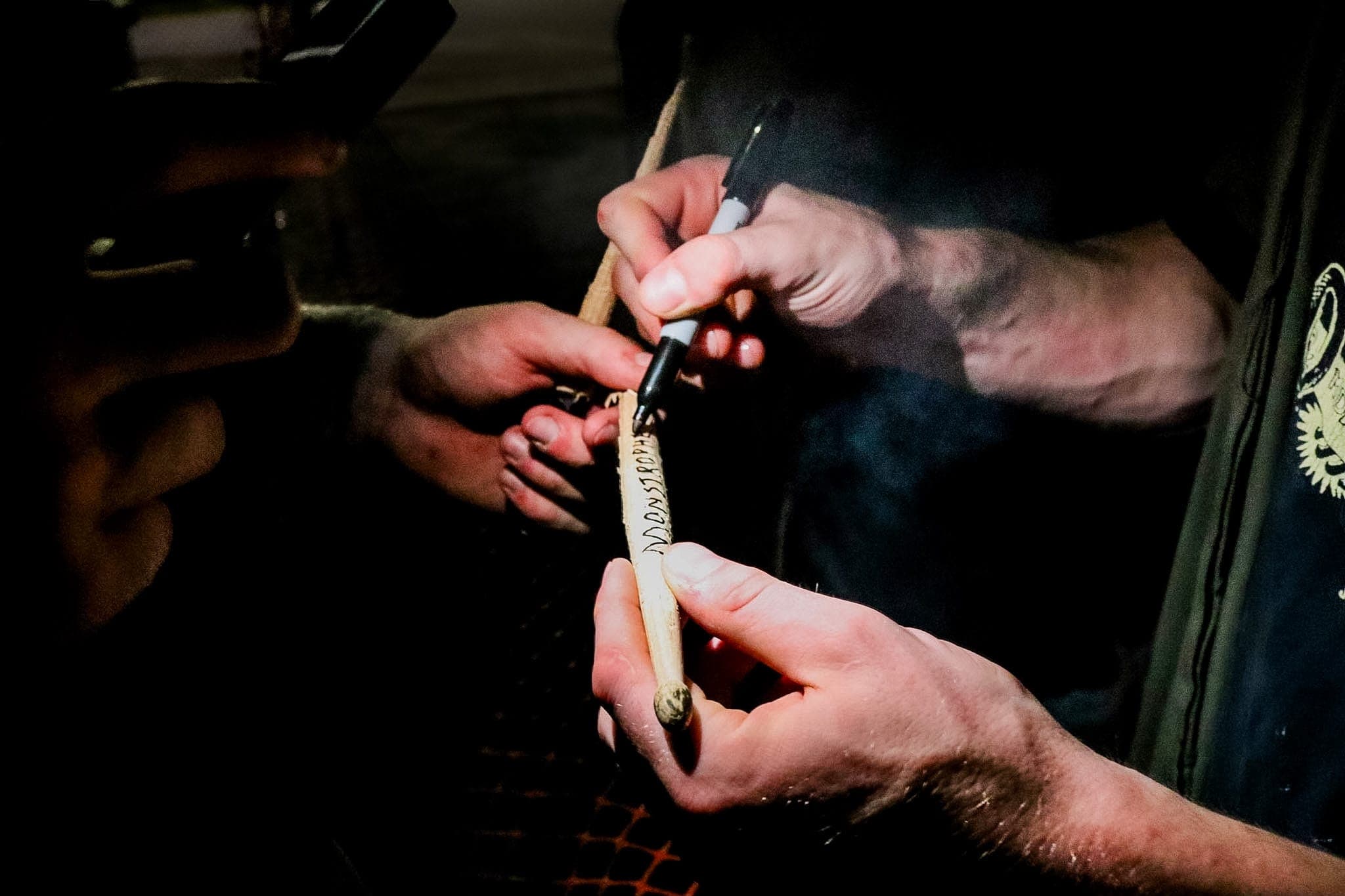Hands signing a drumstick with a marker after the set