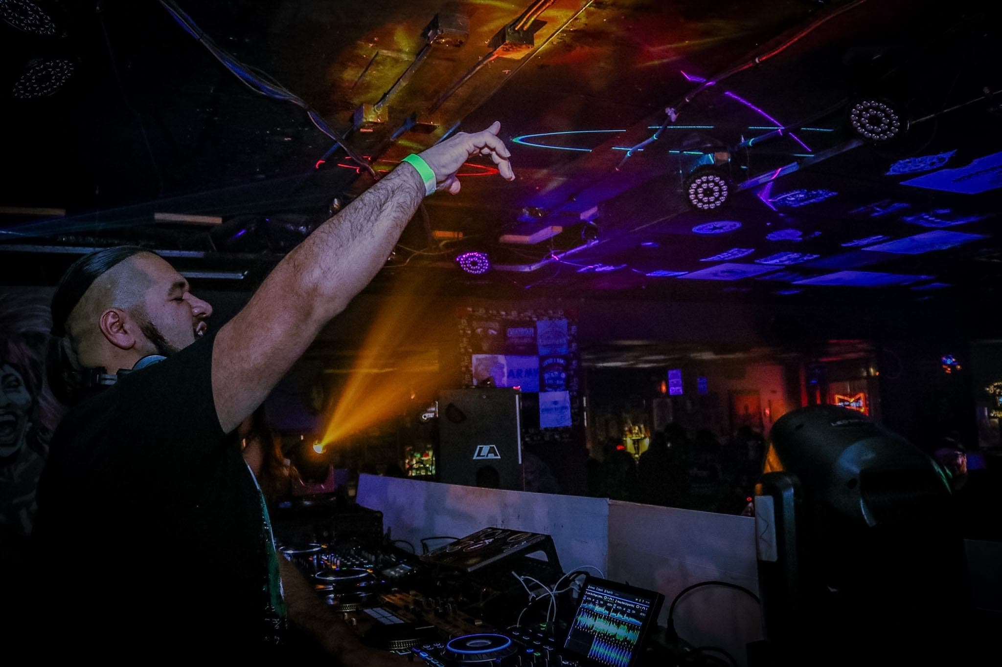 DJ pointing to the ceiling in profile, an orange beam cutting across the club behind him